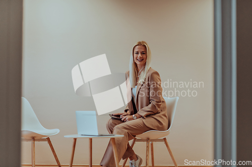 Image of A professional businesswoman sits on a chair, surrounded by a serene beige background, diligently working on her laptop, showcasing dedication and focus in her pursuit of success