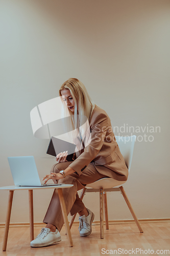 Image of A professional businesswoman sits on a chair, surrounded by a serene beige background, diligently working on her laptop, showcasing dedication and focus in her pursuit of success