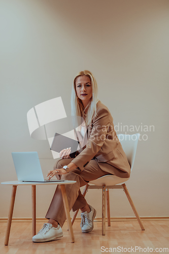 Image of A professional businesswoman sits on a chair, surrounded by a serene beige background, diligently working on her laptop, showcasing dedication and focus in her pursuit of success