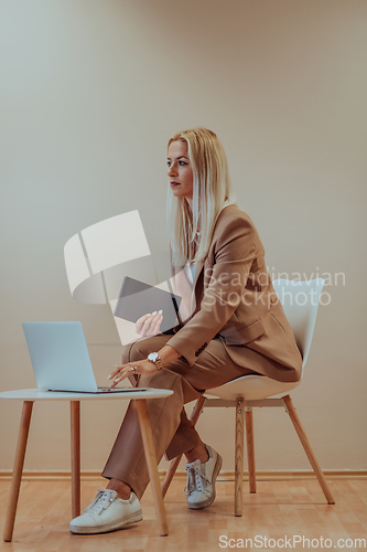 Image of A professional businesswoman sits on a chair, surrounded by a serene beige background, diligently working on her laptop, showcasing dedication and focus in her pursuit of success