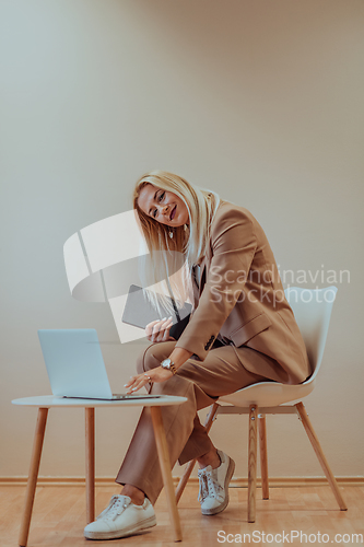 Image of A professional businesswoman sits on a chair, surrounded by a serene beige background, diligently working on her laptop, showcasing dedication and focus in her pursuit of success