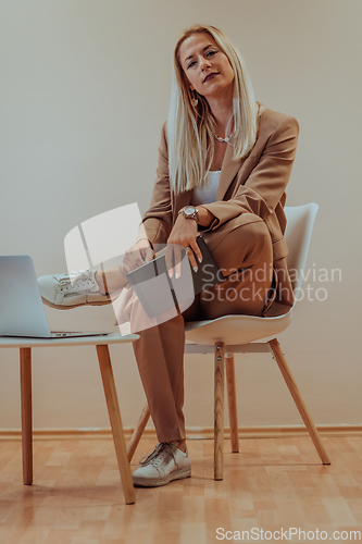 Image of A professional businesswoman sits on a chair, surrounded by a serene beige background, diligently working on her laptop, showcasing dedication and focus in her pursuit of success