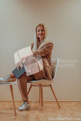 Image of A professional businesswoman sits on a chair, surrounded by a serene beige background, diligently working on her laptop, showcasing dedication and focus in her pursuit of success