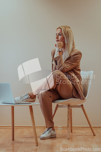 Image of A professional businesswoman sits on a chair, surrounded by a serene beige background, diligently working on her laptop, showcasing dedication and focus in her pursuit of success