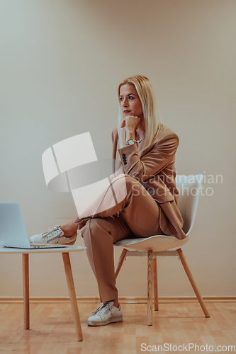 Image of A professional businesswoman sits on a chair, surrounded by a serene beige background, diligently working on her laptop, showcasing dedication and focus in her pursuit of success