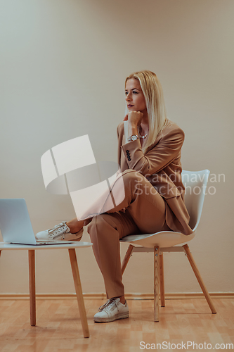 Image of A professional businesswoman sits on a chair, surrounded by a serene beige background, diligently working on her laptop, showcasing dedication and focus in her pursuit of success