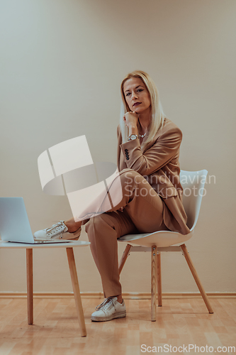 Image of A professional businesswoman sits on a chair, surrounded by a serene beige background, diligently working on her laptop, showcasing dedication and focus in her pursuit of success