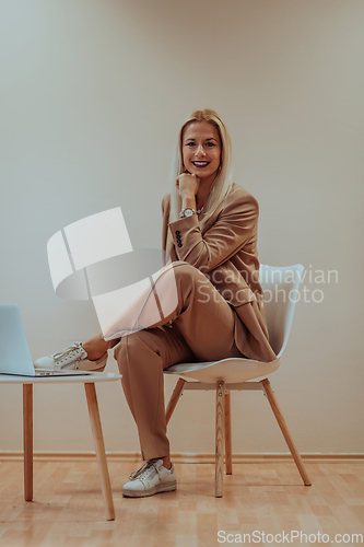 Image of A professional businesswoman sits on a chair, surrounded by a serene beige background, diligently working on her laptop, showcasing dedication and focus in her pursuit of success