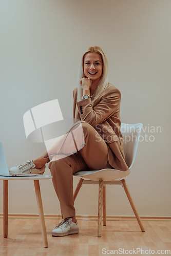 Image of A professional businesswoman sits on a chair, surrounded by a serene beige background, diligently working on her laptop, showcasing dedication and focus in her pursuit of success