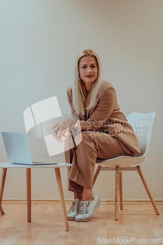 Image of A professional businesswoman sits on a chair, surrounded by a serene beige background, diligently working on her laptop, showcasing dedication and focus in her pursuit of success