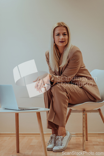 Image of A professional businesswoman sits on a chair, surrounded by a serene beige background, diligently working on her laptop, showcasing dedication and focus in her pursuit of success