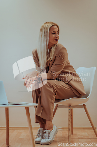 Image of A professional businesswoman sits on a chair, surrounded by a serene beige background, diligently working on her laptop, showcasing dedication and focus in her pursuit of success