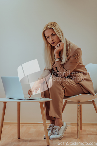 Image of A professional businesswoman sits on a chair, surrounded by a serene beige background, diligently working on her laptop, showcasing dedication and focus in her pursuit of success