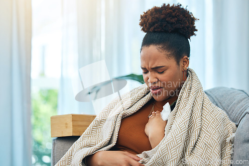 Image of Sick, tissue and chest infection with a black woman on a sofa in the living room of her home to relax. Asthma, allergy or coughing and a young person in a blanket for recovery from cold or flu
