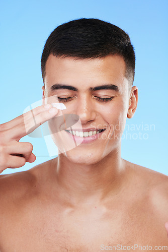 Image of Skincare, beauty and man in a studio with face cream for a health, wellness and self care routine. Cosmetic, dermatology and young male model with facial spf, lotion or sunscreen by a blue background