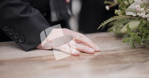 Image of Death, funeral and hand on coffin in mourning, family at service in graveyard or church for respect. Flowers, loss and people at wood casket in cemetery with memory, grief and sadness at grave burial