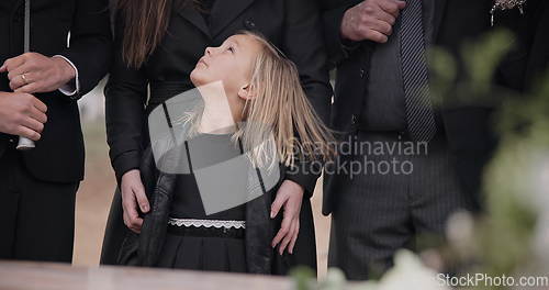 Image of Mourning, grief and family with girl at funeral, flowers on coffin, death and sad child at service in graveyard. Support, loss and people at casket in cemetery with kid crying at grave for burial.