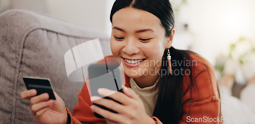 Image of Asian woman, credit card and phone relaxing on her sofa online shopping, ecommerce and fintech easy payment. Young person in China typing bank information on cellphone for finance transaction at home