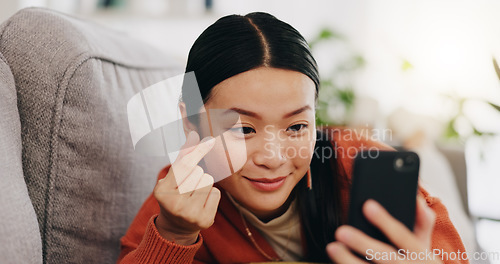 Image of Asian woman, selfie and lying on sofa with heart sign and love for profile picture, vlog or social media at home. Happy female relaxing with smile and hand signs for photo or online vlogging on couch