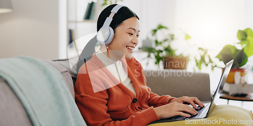 Image of Laptop, headphones and asian woman on couch with work from home opportunity in online or website copywriting. Remote worker or person in china typing on her computer and listening to music at home