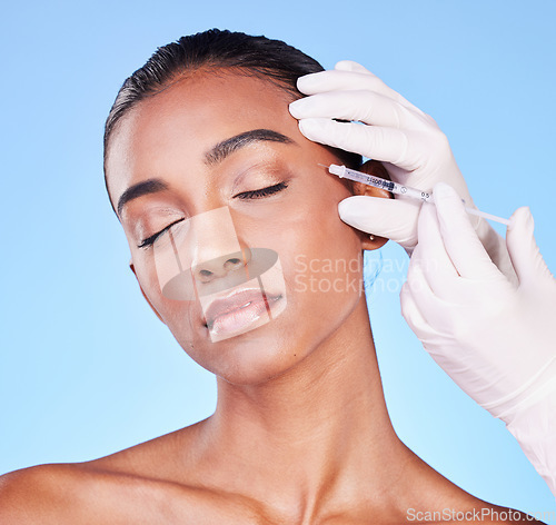 Image of Needle, woman and face in studio for skincare, beauty process and aesthetic filler on blue background. Indian model, hands of surgeon and injection for plastic surgery, facial change or prp cosmetics