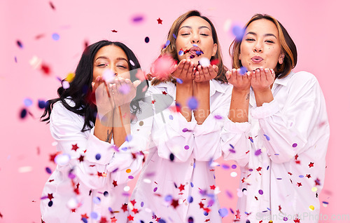 Image of Blowing confetti, friends and women in studio for party celebration, fashion sale and discount. Bonding, diversity and happy people on pink background for support, natural beauty and retail promotion