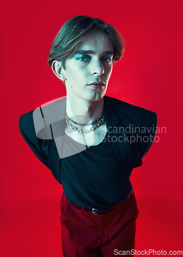 Image of Fashion, lgbtq and portrait of a man in a studio with beauty face. stylish and classy outfit. Makeup, queer and young gay male model with funky, edgy and cool style isolated by a red background.
