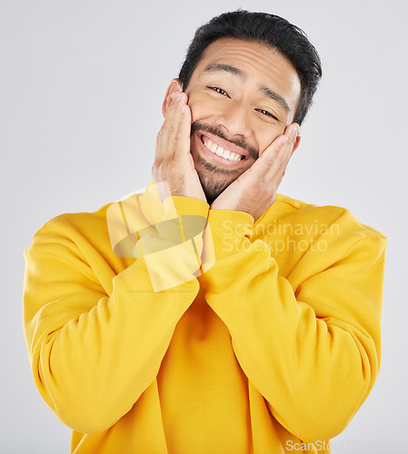 Image of Smile, shy and hands on face of asian man in studio for in love, sweet or gesture on grey background. Happy, portrait and Japanese male model pose with emoji cheeks expression for romantic sign