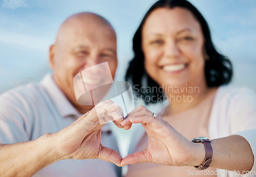 Image of Heart shape, hands and mature couple at the beach on a romantic vacation, adventure or holiday. Smile, emoji and portrait of man and woman in retirement with love or support gesture by ocean on trip.