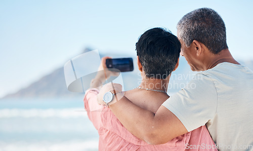 Image of Beach, photography and back of elderly couple hug in nature for travel, freedom and photo memory. Smartphone, profile picture and rear view of seniors at sea for retirement trip, selfie or vacation