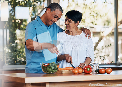 Image of Happy couple, love and hug while cooking food, cutting carrot and prepare vegetables for salad at home. Mature man, smile and embrace woman in kitchen to make healthy lunch, meal and diet for dinner