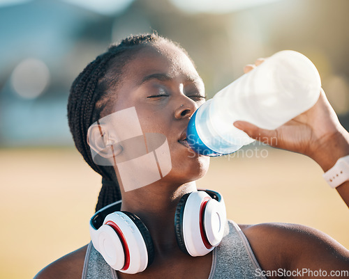 Image of Black woman, drinking water and health, fitness and runner outdoor with headphones, thirsty after workout with cardio. Bottle, hydration and h2o, exercise and wellness with athlete, music and sports