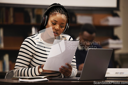 Image of Woman, documents and headphones in library for research, studying and computer research or planning in university. African student reading paper, listening to music and laptop for focus and learning