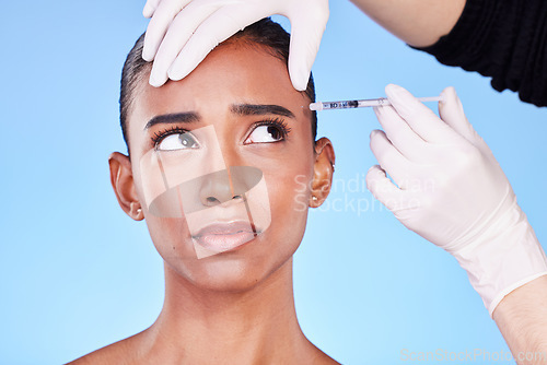 Image of Injection, hands and face of Indian woman for plastic surgery, cosmetics and skincare in studio. Dermatology needle, anxiety and surgeon and person for anti aging, botox and beauty on blue background