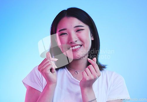 Image of Love, hands and portrait of Asian woman in studio with smile for romance, valentines day and happy. Emoji, neon lighting and face of person with hand gesture, finger sign or symbol on blue background