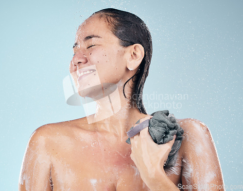 Image of Clean, woman and shower with water, soap and sponge for healthy dermatology, skincare and blue background in studio. Person, smile and washing skin and body with foam bubbles in bathroom