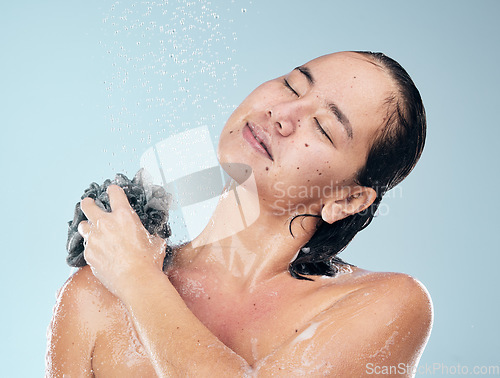 Image of Woman, shower and water drops with loofah in hygiene, grooming or washing against a blue studio background. Female person in relax for body wash, cleaning or skincare routine under rain in bathroom