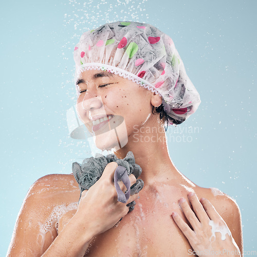 Image of Happy woman, shower and water drops with loofah in hygiene, grooming or washing against a blue studio background. Female person in relax body wash, cleaning or skincare routine under rain in bathroom