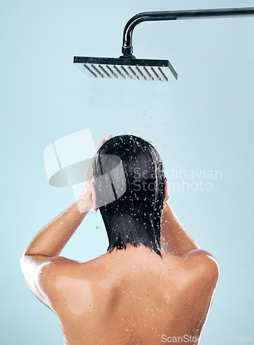 Image of Woman, shower and back in water drops for hygiene, grooming or washing against a blue studio background. Rear view of female person in body wash, cleaning or skincare routine under rain in bathroom
