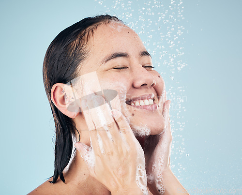 Image of Skincare, shower soap and happy woman cleaning in studio isolated on a blue background. Water splash, hygiene foam and model smile, washing and bathing in wellness, healthy skin or beauty in bathroom