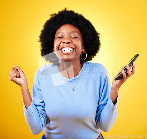 Image of Woman, phone and fist for success in studio, celebration and winning lottery prize, promotion or bonus on yellow background. Happy african model, mobile app and celebrate online gambling achievement