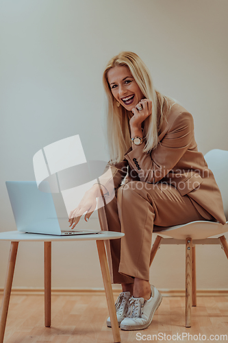 Image of A professional businesswoman sits on a chair, surrounded by a serene beige background, diligently working on her laptop, showcasing dedication and focus in her pursuit of success