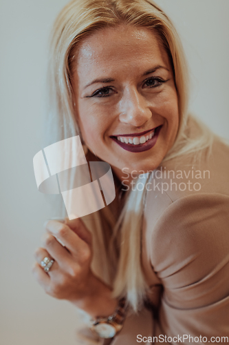 Image of A confident and successful businesswoman, with a wide smile, strikes a pose in front of a beige background, exuding professionalism and elegance