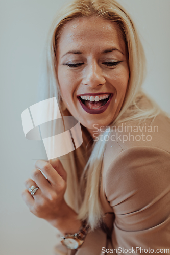 Image of A confident and successful businesswoman, with a wide smile, strikes a pose in front of a beige background, exuding professionalism and elegance