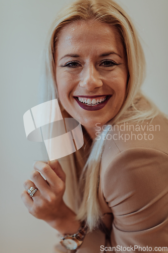 Image of A confident and successful businesswoman, with a wide smile, strikes a pose in front of a beige background, exuding professionalism and elegance