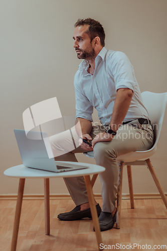 Image of A confident businessman sitting and using laptop with a determined expression, while a beige background enhances the professional atmosphere, showcasing his productivity and expertise.