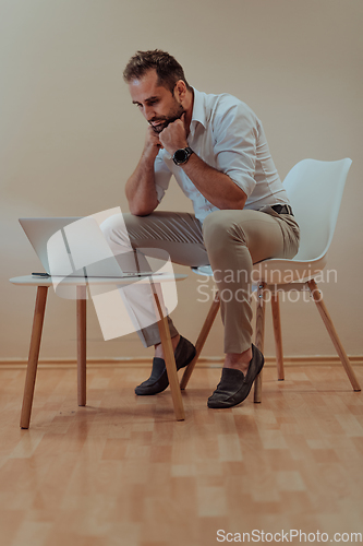 Image of A confident businessman sitting and using laptop with a determined expression, while a beige background enhances the professional atmosphere, showcasing his productivity and expertise.