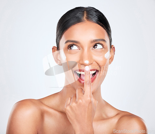 Image of Cream, woman and facial cosmetics in studio for aesthetic skincare, dermatology or smile on white background. Happy indian model, face lotion and thinking of beauty, sunscreen and healthy moisturizer