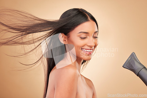 Image of Beauty, hairdryer and young woman in a studio with salon keratin treatment for wellness. Hair care, cosmetic and Indian female model with cosmetology tool for hairstyle isolated by a brown background