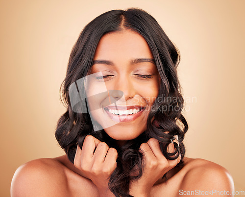 Image of Hair care, happy and young woman in a studio with healthy salon keratin treatment for wellness. Beauty, cosmetic and headshot of Indian female model with hairstyle isolated by a brown background.